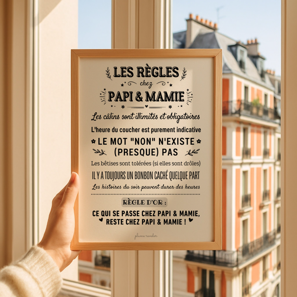 Affiche « Les règles chez Papi & Mamie » dans un cadre en bois, tenue devant une fenêtre.