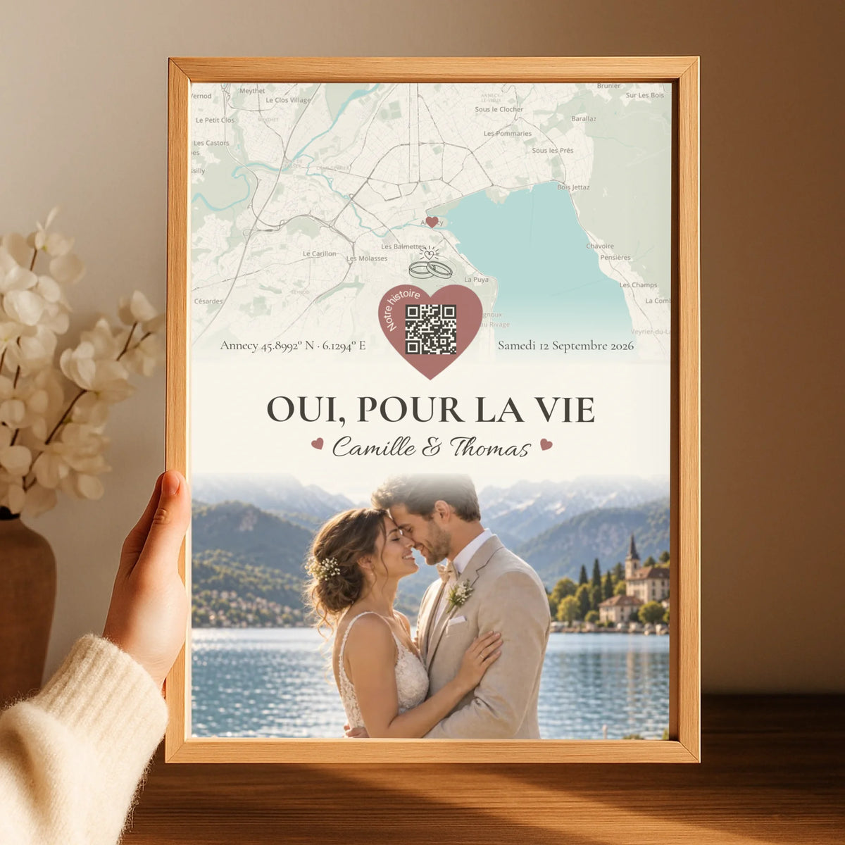 Affiche mariage personnalisée tenue à la main dans un cadre en bois, avec carte et photo des mariés.