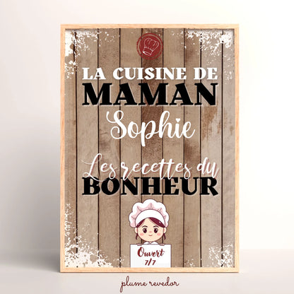 Affiche La cuisine de Maman avec prénom, fond effet bois et petite cuisinière illustrée, présentée dans un cadre.