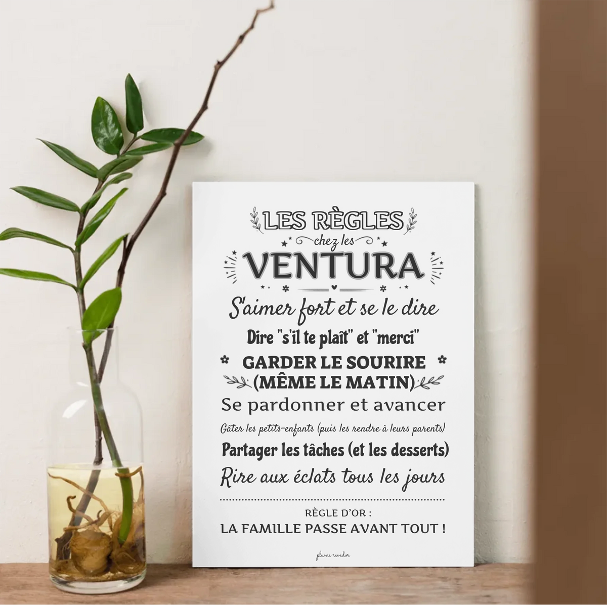 Affiche des règles de la famille Ventura posée sur une étagère, près d’un vase avec une branche.
