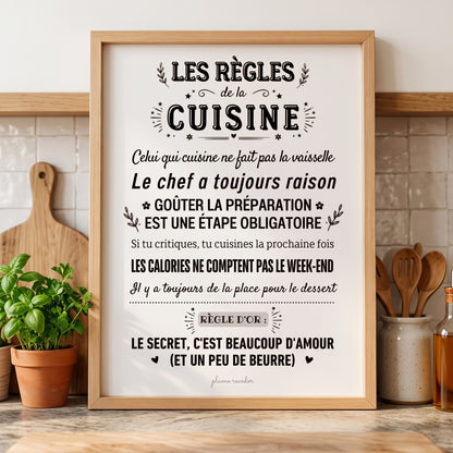 Affiche « Les règles de la cuisine » dans un cadre en bois, sur un plan de travail avec des herbes et des ustensiles.