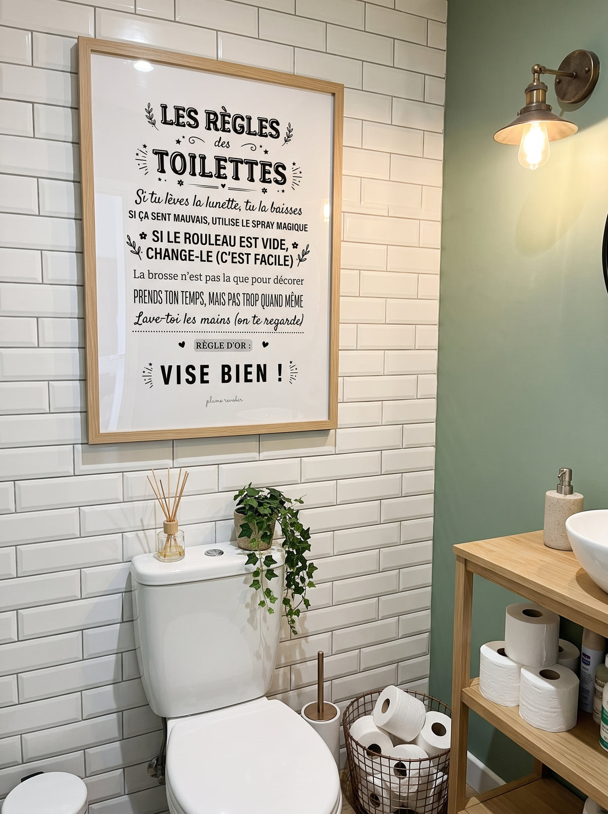 Affiche « Les règles des toilettes » dans un cadre clair, au-dessus des WC sur un mur en carrelage blanc.