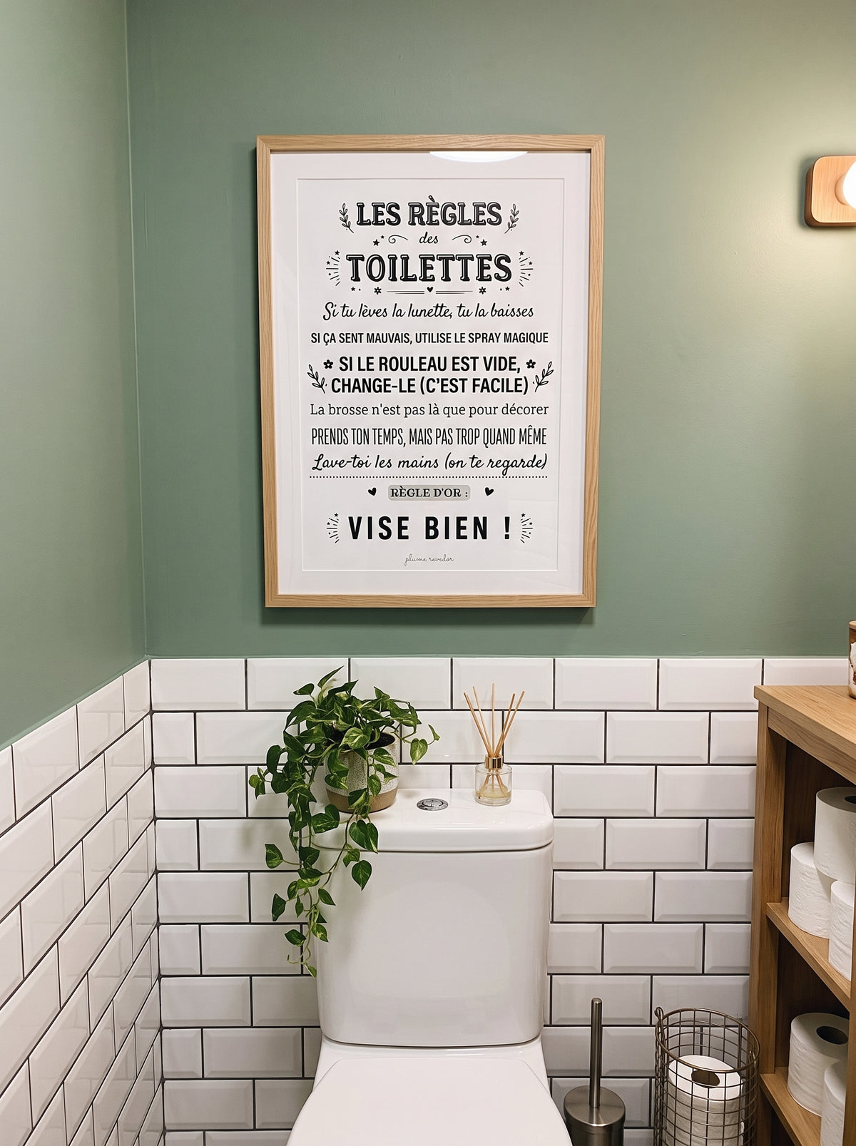 Affiche « Les règles des toilettes » encadrée au-dessus des WC, sur un mur vert avec du carrelage blanc.