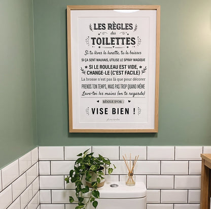Affiche « Les règles des toilettes » encadrée au-dessus des WC, sur un mur vert avec du carrelage blanc.