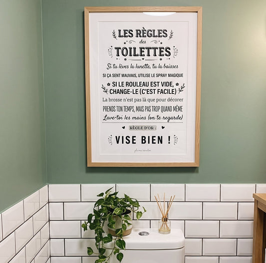 Affiche « Les règles des toilettes » encadrée au-dessus des WC, sur un mur vert avec du carrelage blanc.