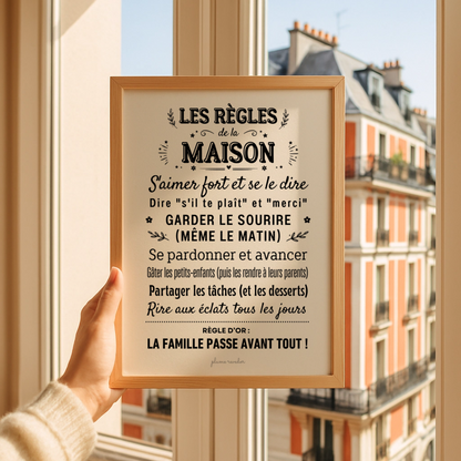 Affiche « Les règles de la maison » dans un cadre en bois, tenue devant une fenêtre donnant sur la ville.