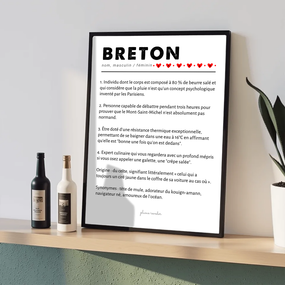 Affiche Breton dans un cadre noir posé sur une étagère, entre deux bouteilles et une plante.